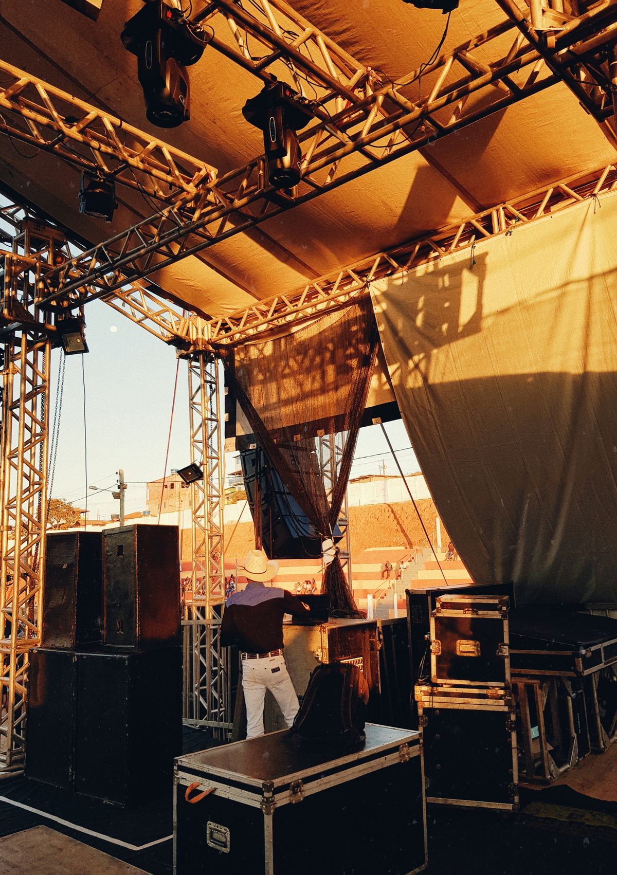Technician checking equipment among trusses and cases on an outdoor stage